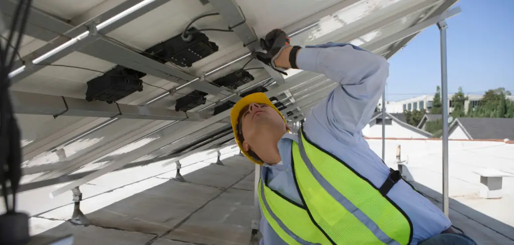Solar panel expert performing maintenance on the underside of several solar panels.