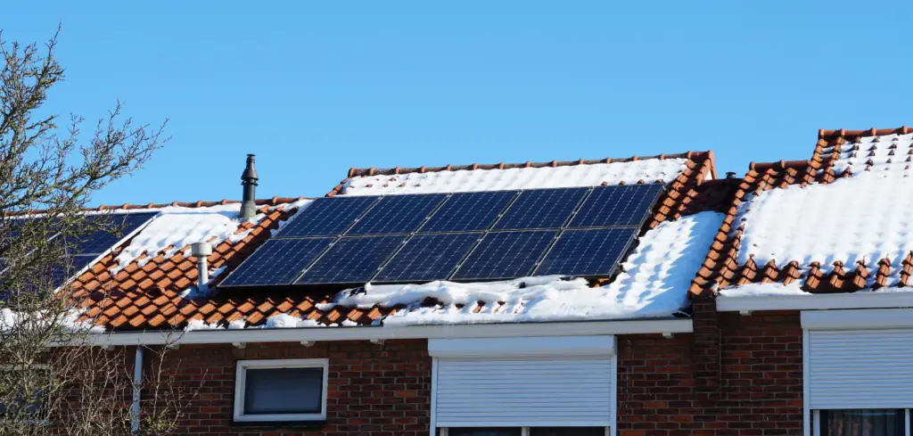 A set of solar panels on the roof of a home but they are covered in a layer of snow.