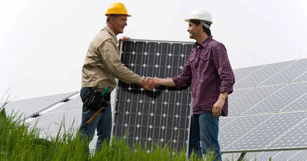 Two men shaking hands in front of large solar panel