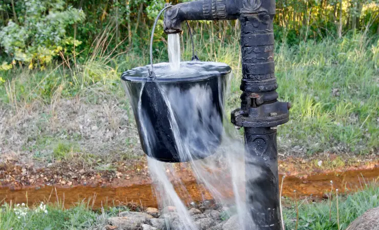 Black bucket overflowing from water coming out of well pump