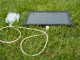 Solar trickle charger charging a phone outdoor on green grass