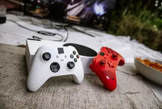 Xbox console located outdoors with one white controller on the left and a red controller on the right.