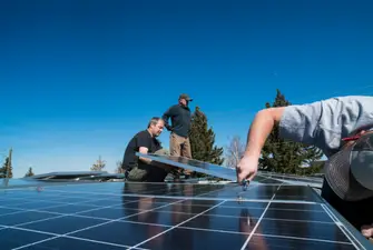 Three men on a roof improving solar panel performance by realigning them.