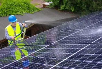 A man spraying water with a hose on solar panels after using isopropyl alcohol to clean them.
